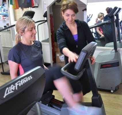 A Female Personal Trainer Helping A Woman On A Machine In The Gym